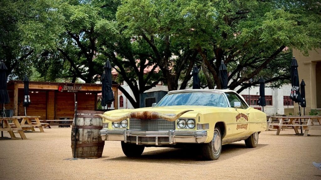 Vintage yellow car with longhorn hood ornament in outdoor plaza, Fort Worth, Texas.