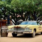 Vintage yellow car with longhorn hood ornament in outdoor plaza, Fort Worth, Texas.