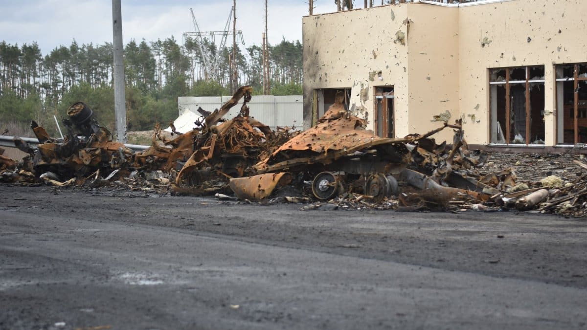 A dramatic scene depicting the aftermath of destruction with burnt vehicles and damaged building exterior.
