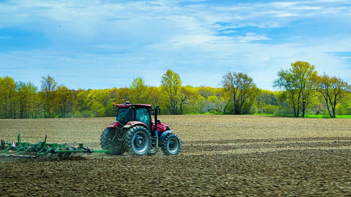 A vibrant red tractor plowing a field under a bright blue sky. Ideal for agricultural themes.
