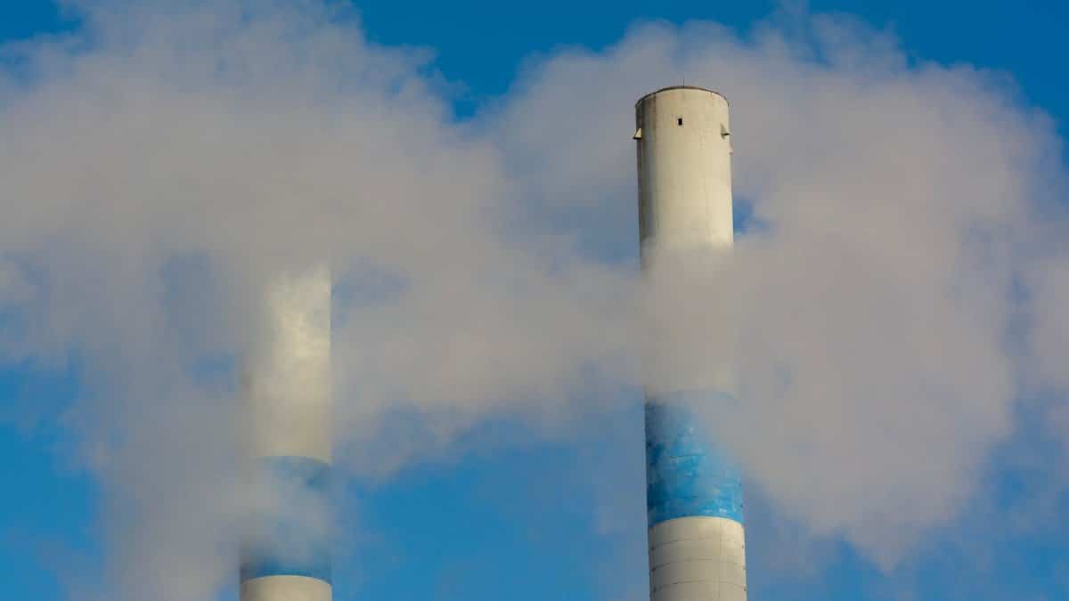 Twin industrial chimneys emitting smoke under a clear blue sky, highlighting air pollution concerns.