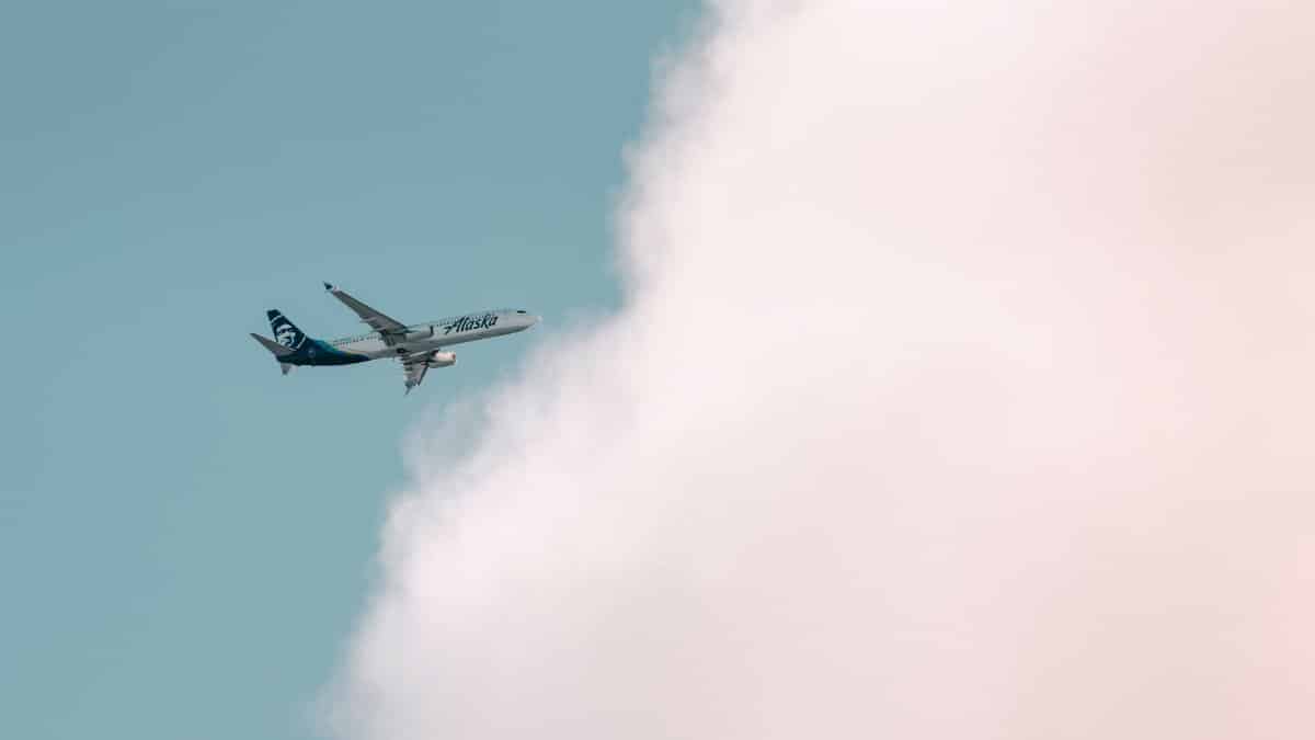 Alaska Airlines plane soaring through a bright sky with fluffy clouds in Seattle.