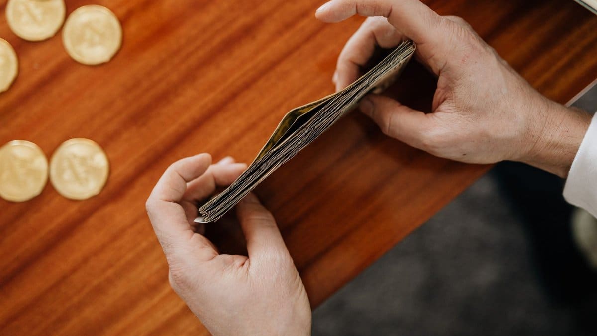 Close-up of hands counting currency with coins scattered on a wooden table. Perfect for finance and business themes.