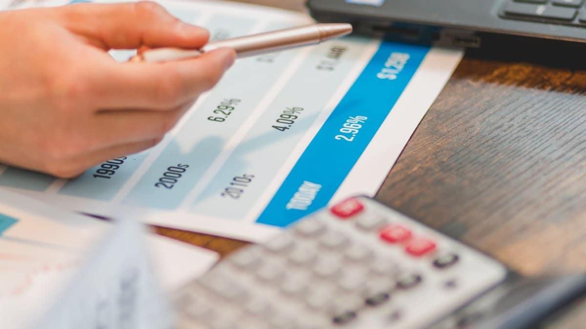 Close-up of a hand using a ballpen and calculator to analyze interest rates on a chart.