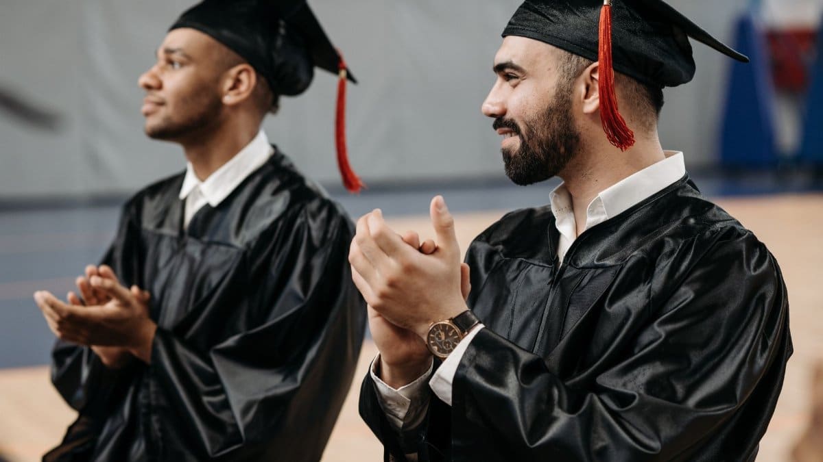 Two graduates clapping and celebrating their achievements in caps and gowns during a graduation ceremony.