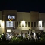 Amazon warehouse building illuminated at night with trees and signage.