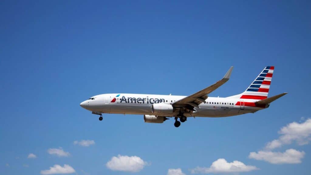 An American Airlines plane flying through a clear blue sky, showcasing aviation travel.