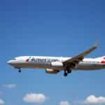 An American Airlines plane flying through a clear blue sky, showcasing aviation travel.