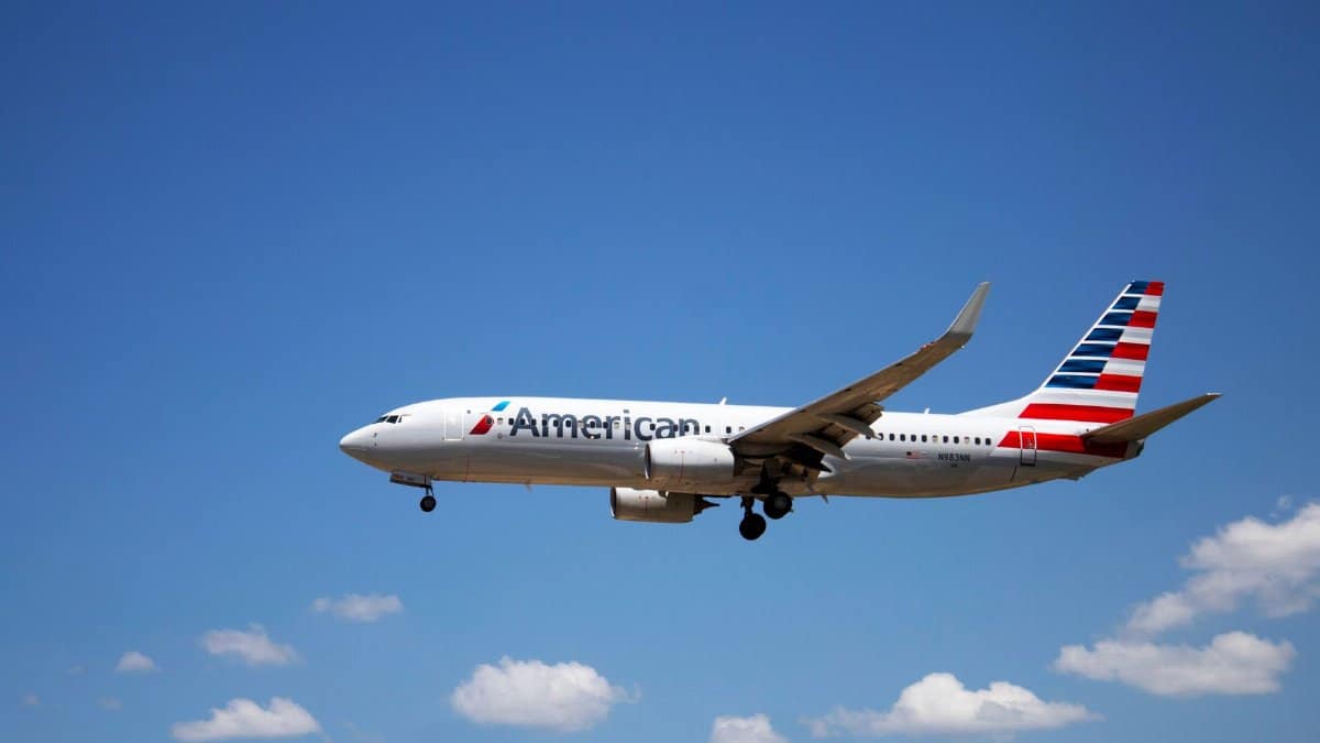 An American Airlines plane flying through a clear blue sky, showcasing aviation travel.