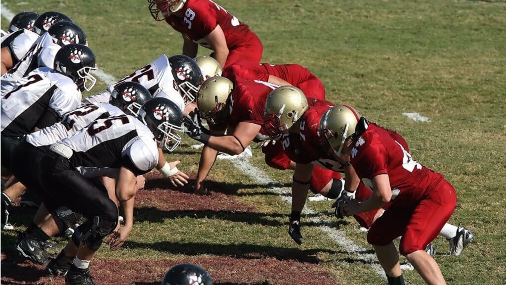Intense moment as two American football teams face off at the line of scrimmage on a sunny day.