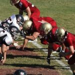 Intense moment as two American football teams face off at the line of scrimmage on a sunny day.