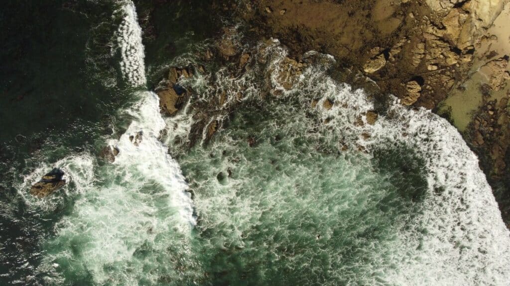 Top-down view of ocean waves crashing on a rocky shore at Newport Beach, California.