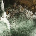 Top-down view of ocean waves crashing on a rocky shore at Newport Beach, California.