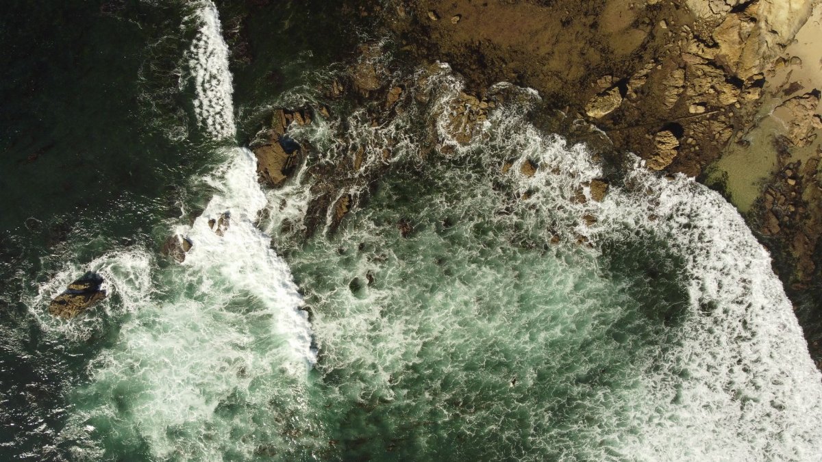 Top-down view of ocean waves crashing on a rocky shore at Newport Beach, California.