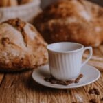 Artistic arrangement of fresh bread and a coffee cup on a rustic wooden table with scattered coffee beans.