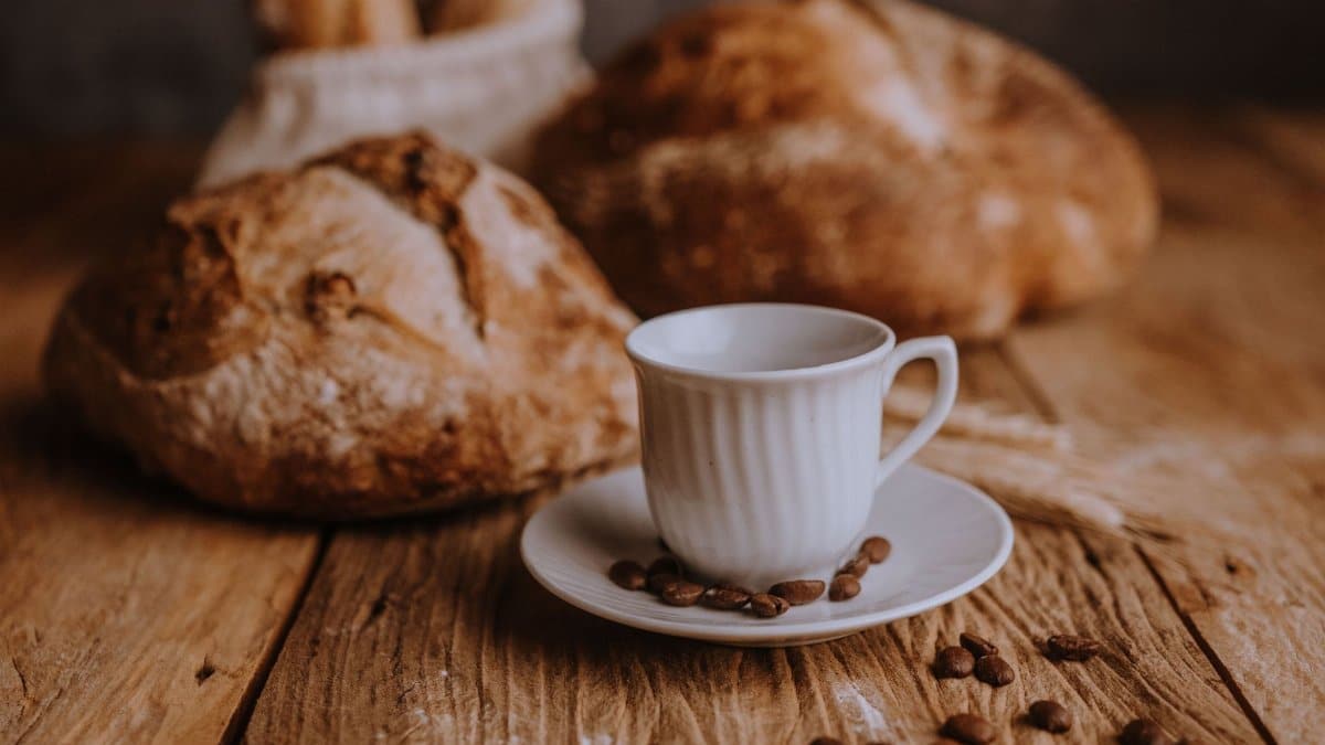 Artistic arrangement of fresh bread and a coffee cup on a rustic wooden table with scattered coffee beans.