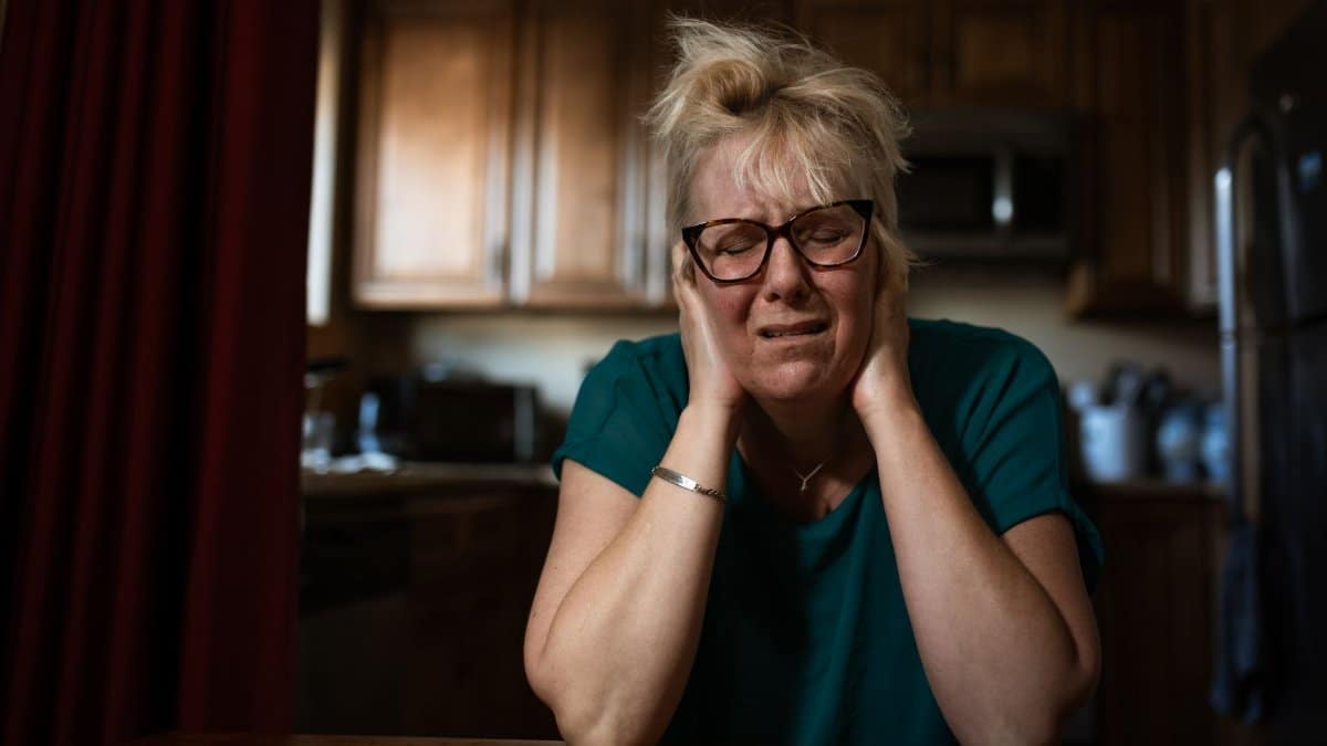 An adult woman in distress sitting at a table indoors, conveying emotional struggle.