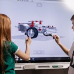 A boy and girl collaborate on a robotics project using a digital screen in a classroom setting.