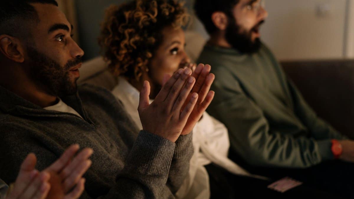 Diverse group of adults clapping with anticipation indoors, reflecting joy and engagement in a cozy setting.