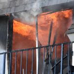 A blazing fire erupts from an apartment window, showcasing dramatic flames and smoke.