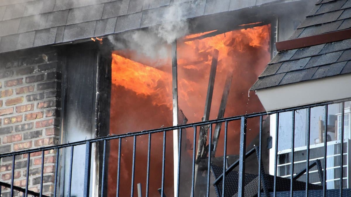 A blazing fire erupts from an apartment window, showcasing dramatic flames and smoke.