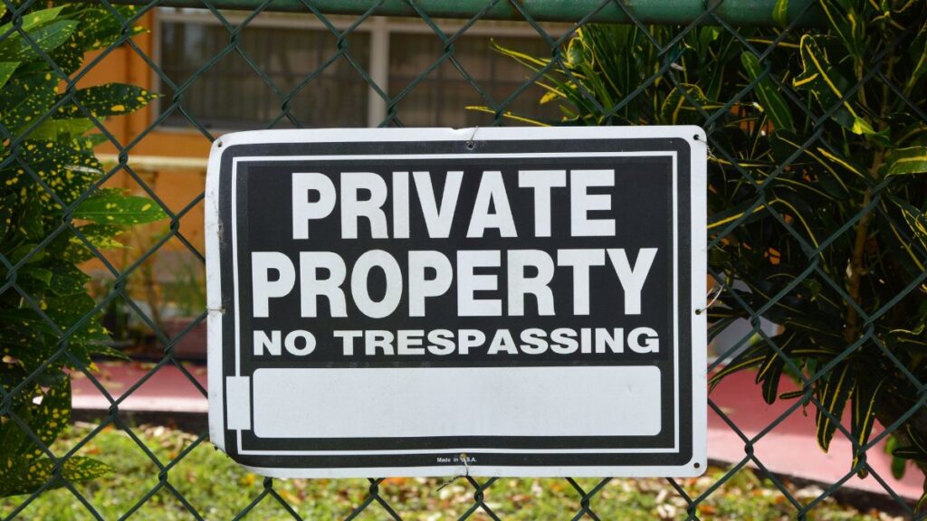 Close-up of a private property no trespassing sign on a chain-link fence with greenery in the background.