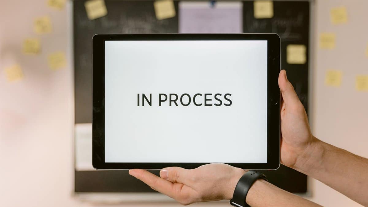 Close-up of hands holding a tablet displaying 'In Process' text, emphasizing workflow.