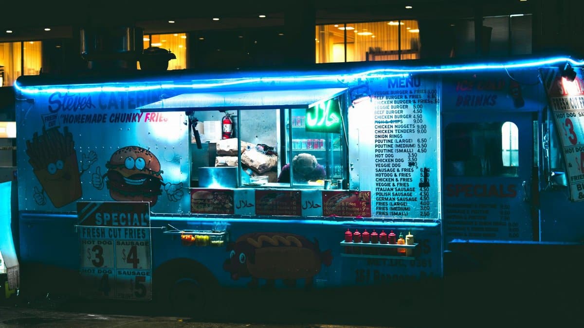 A vibrant food truck illuminated with neon lights at night, offering a variety of street food options.
