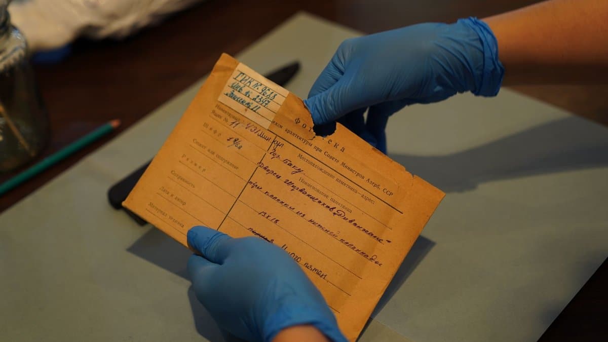 Archival document being carefully handled with blue gloves at a desk.
