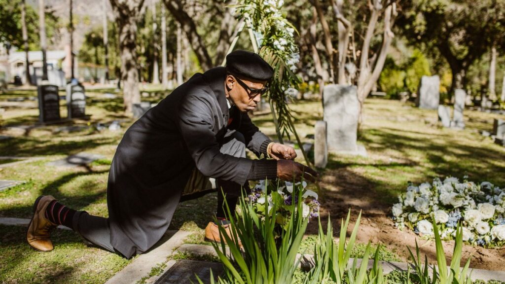 A man kneeling and attending to a grave at a sunlit cemetery.