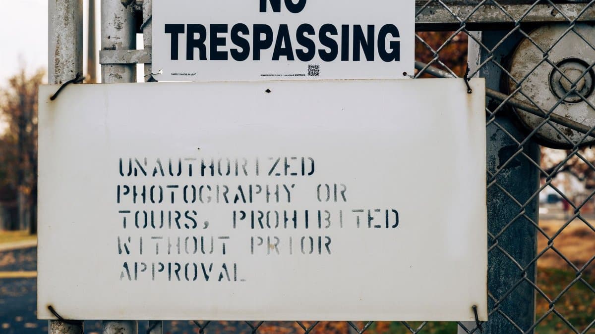 A warning sign on a metal fence prohibiting trespassing and unauthorized activities.