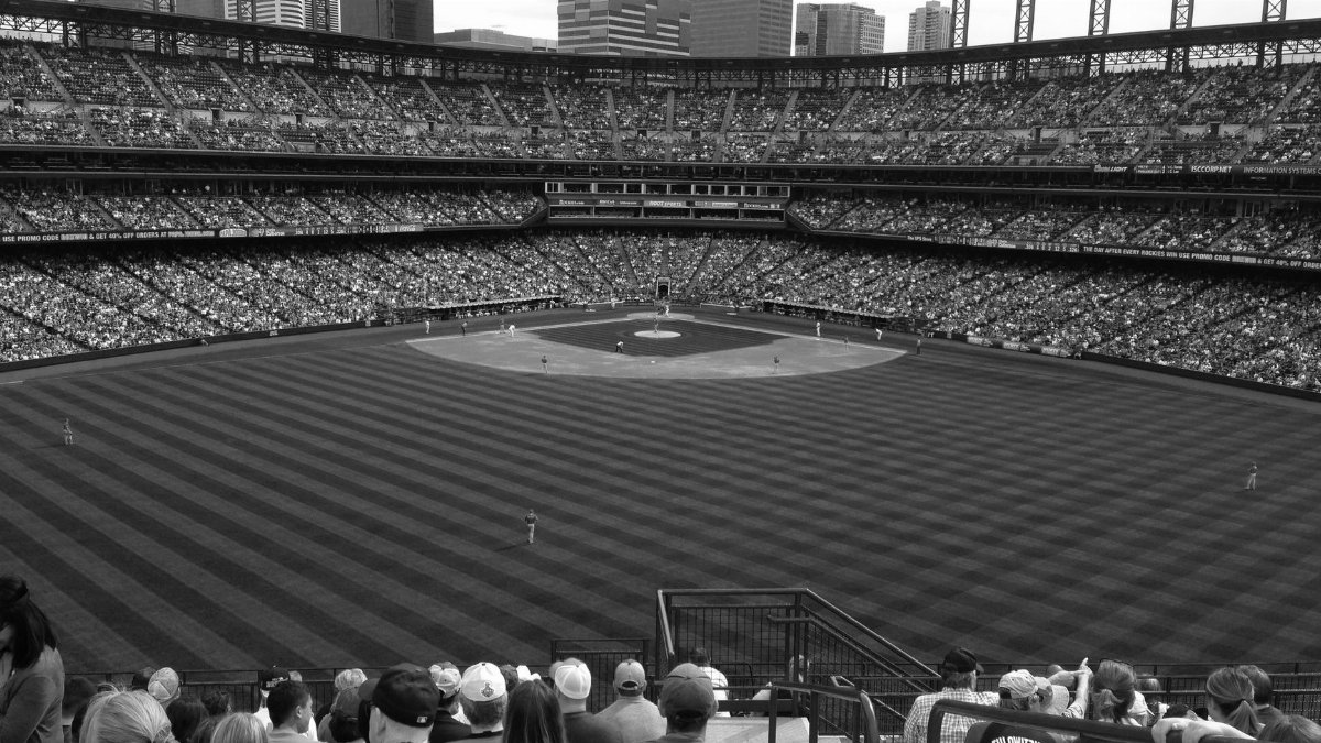 Black and white image of a crowded baseball game at Coors Field, Denver with city skyline in background.