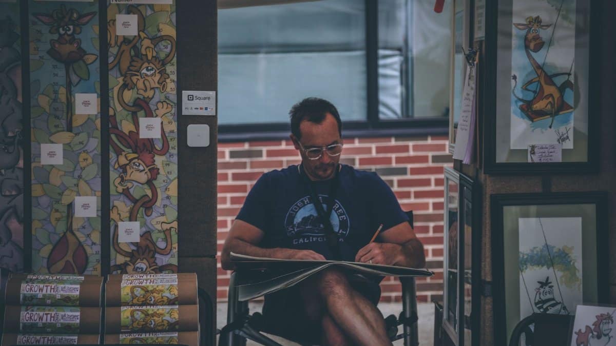 Captured moment of a street artist sketching in an outdoor art booth with colorful designs.