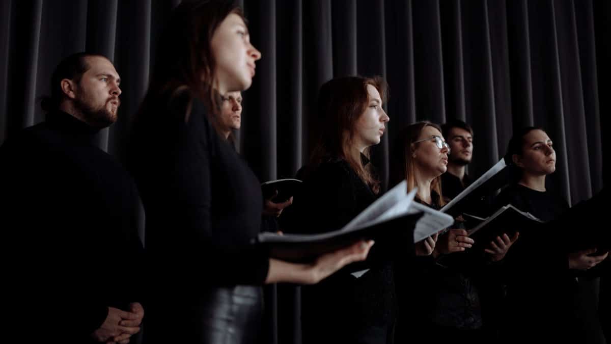 Choir singers in black clothing performing with music sheets indoors, captured from a low angle.