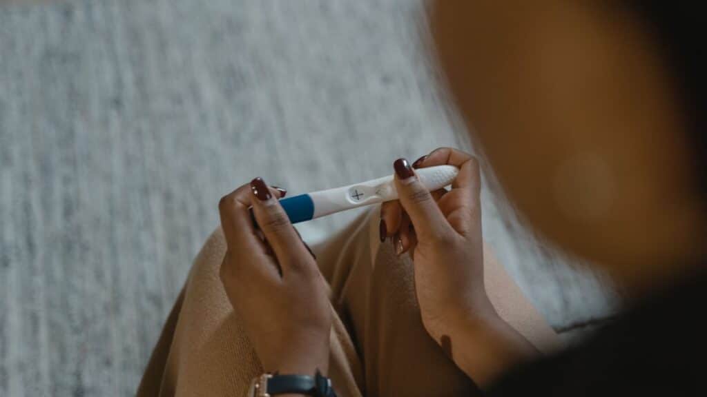 Close-up of a woman holding a positive pregnancy test with a plus sign, symbolizing new beginnings.
