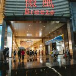 A bustling shopping mall entrance with people and umbrellas on a rainy evening.