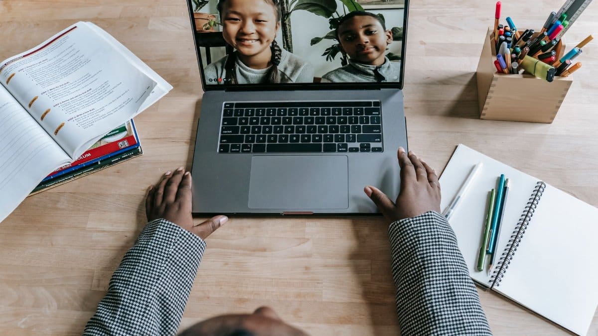 Crop anonymous clever African American female talking with pupils about plan of homework online on laptop