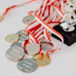 A varied collection of silver and gold medals alongside trophies on a white surface, showcasing achievement.