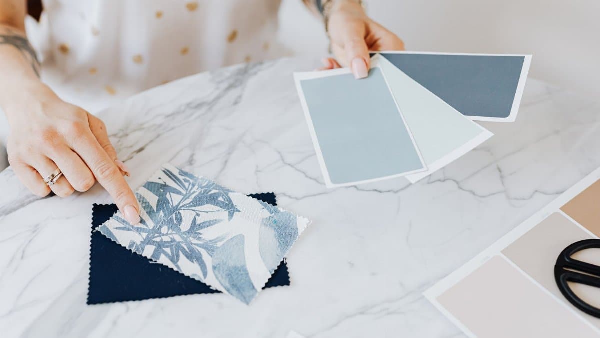 Woman selecting color and fabric swatches on marble desk for interior design project.