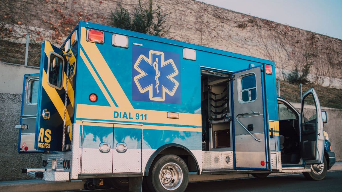 Blue ambulance parked on roadside with open doors, emergency medical service vehicle.
