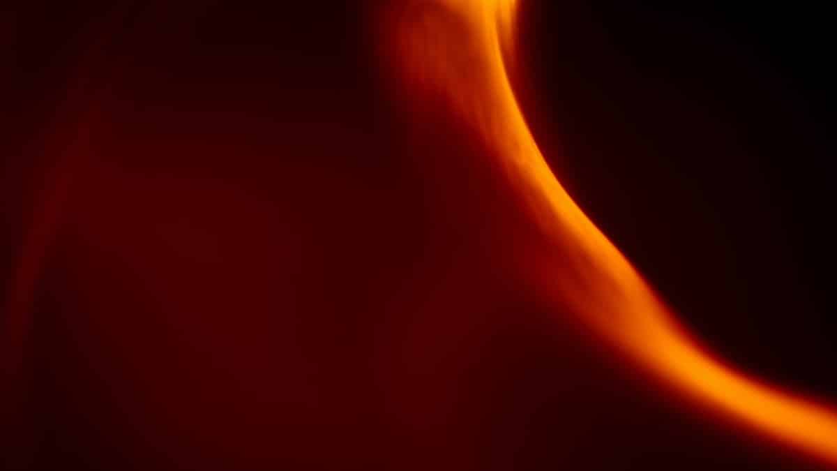 Dynamic abstract art featuring an orange flame-like light pattern against a dark background.