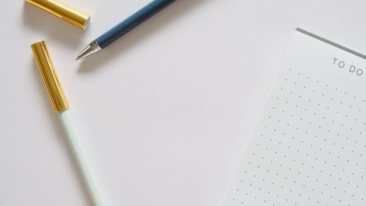A minimalist flat lay featuring a to-do list notebook and pens on a white background.