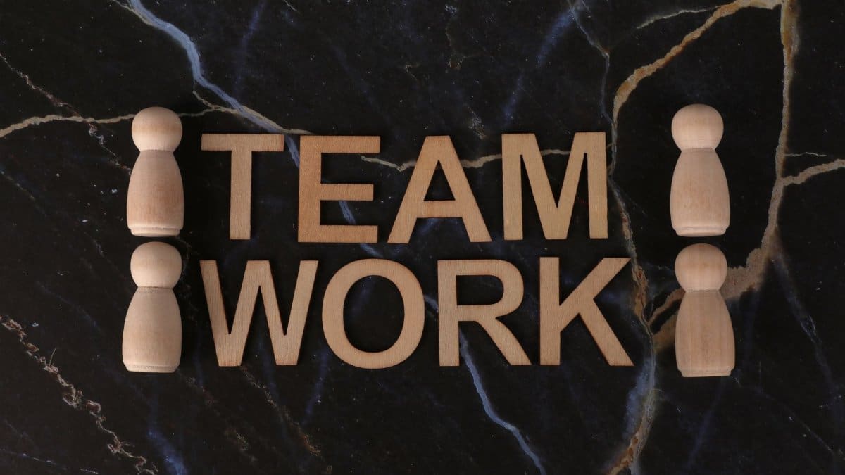 Wooden figures symbolize teamwork on a dark marble background, emphasizing collaboration.