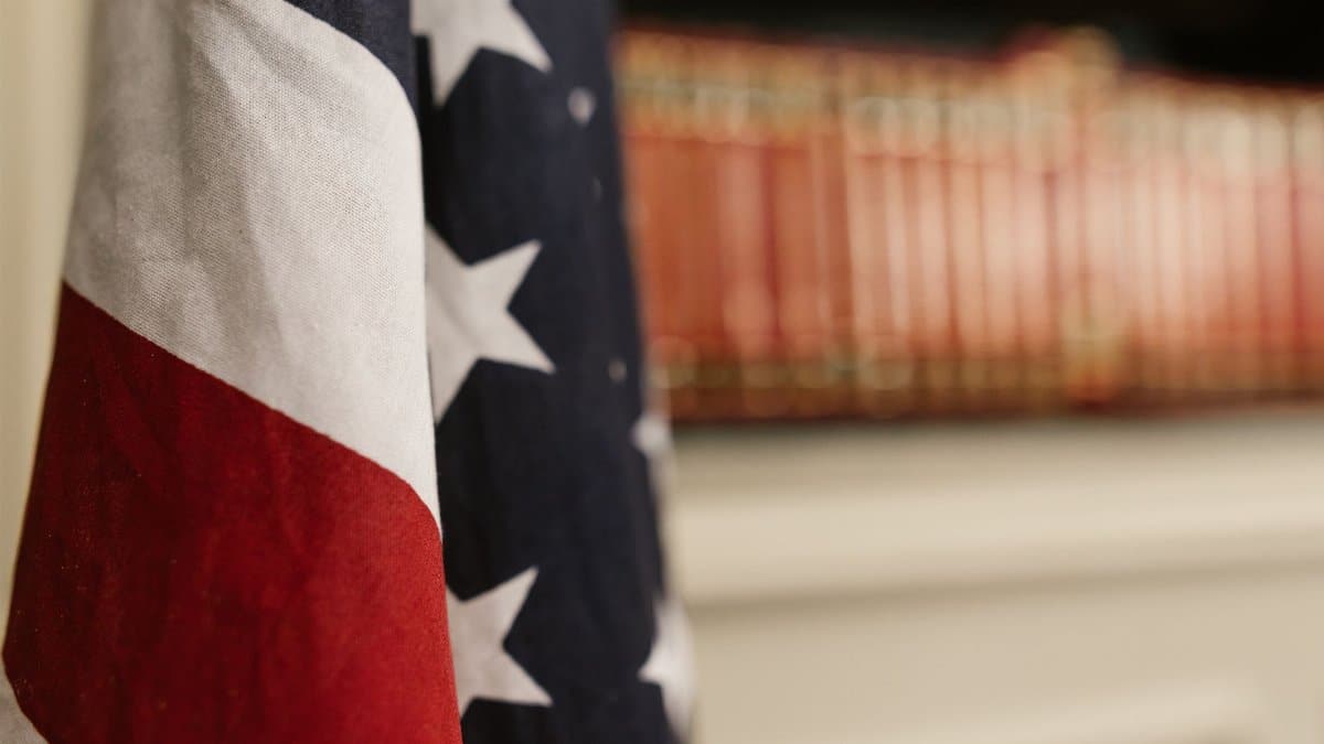 Detailed close-up of an American flag indoors with blurred bookshelf in the background.