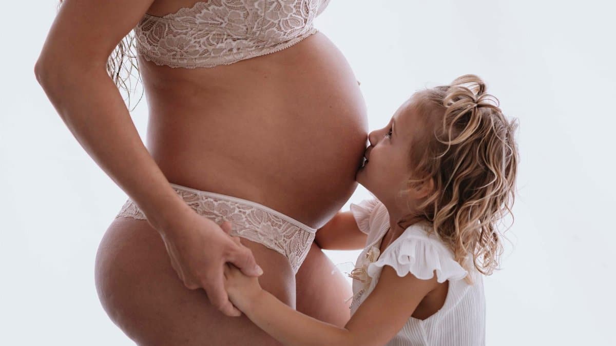 Child kissing pregnant mother's belly, symbolizing love and anticipation of a new family member.