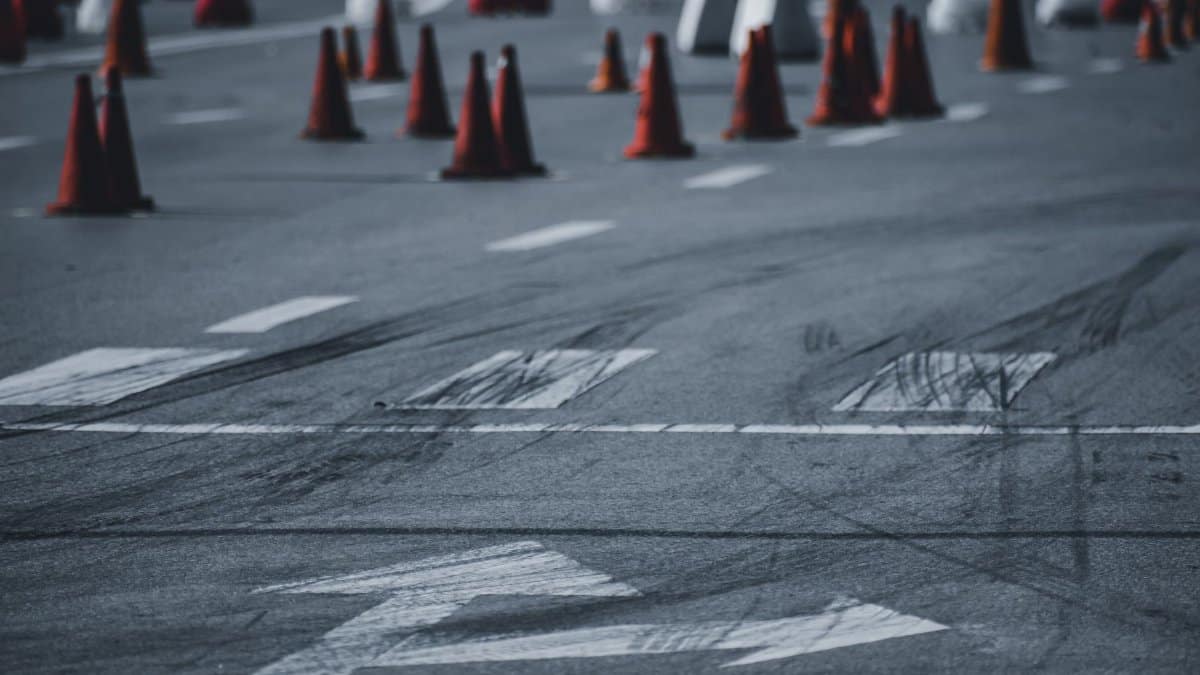 Asphalt roadway with black wheel tracks and red road cones placed on city street in daytime