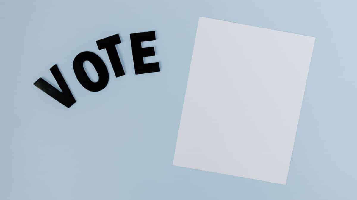 Flat lay of blank paper with 'VOTE' letters on light blue background, ideal for election-themed content.