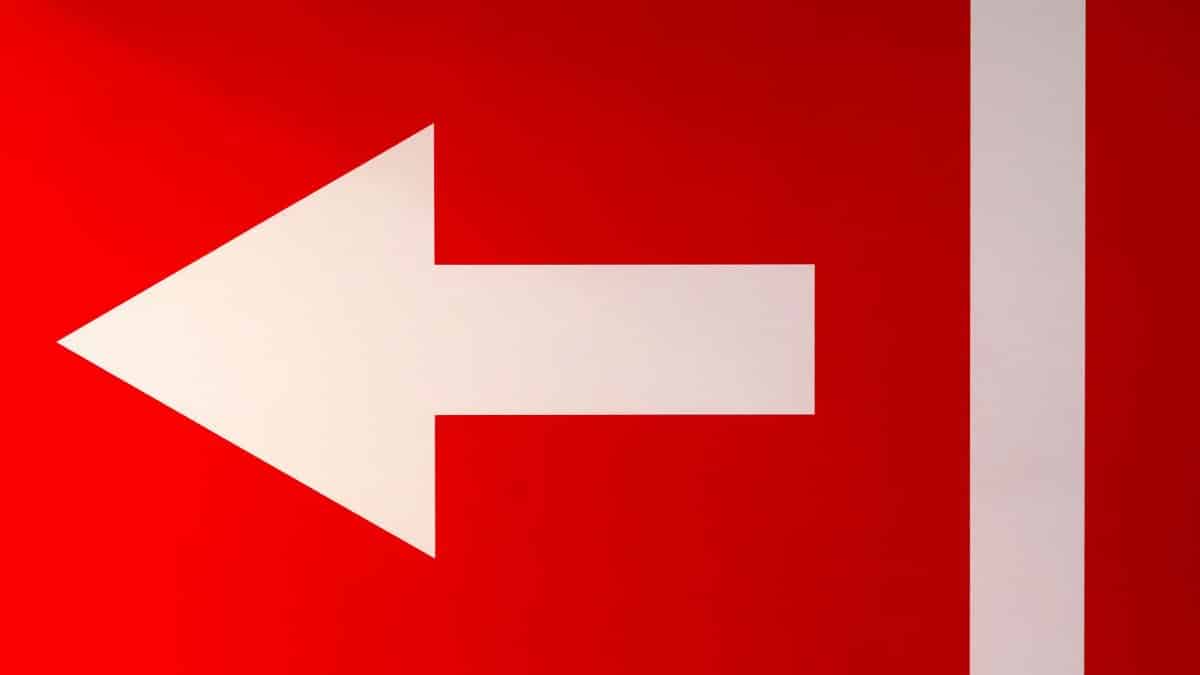 White arrow pointing left on a bold red background, symbolizing direction.