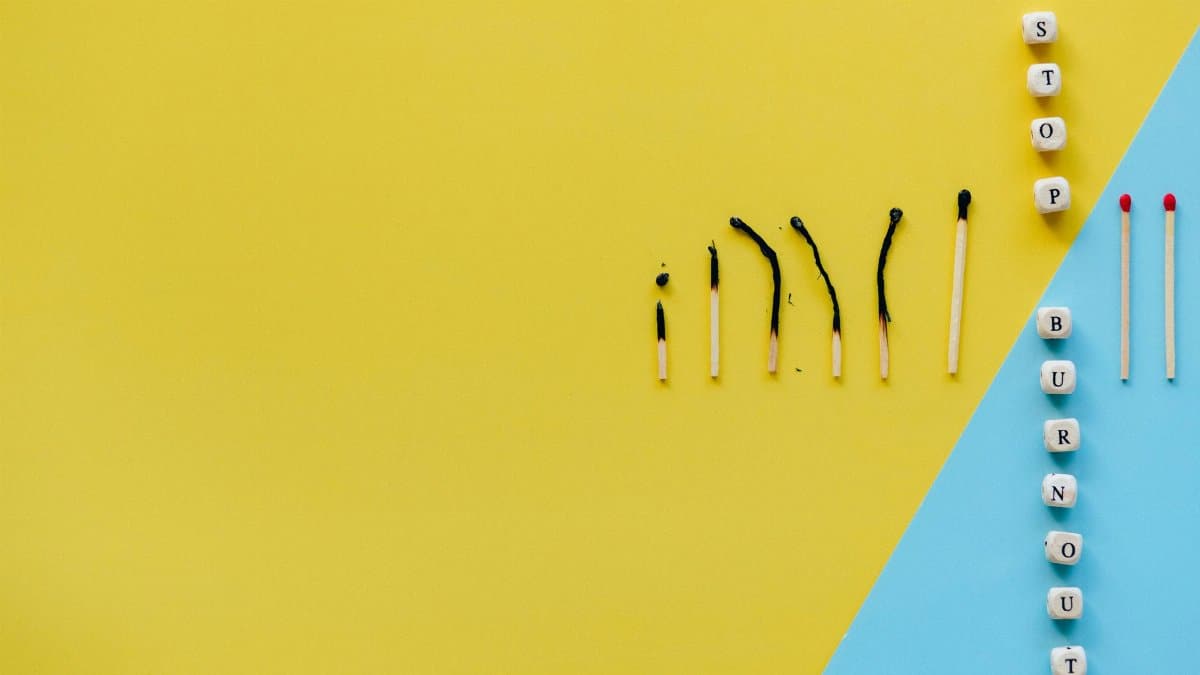Artistic representation of burnout using matches and blocks spelling 'STOP BURNOUT' on colorful background.