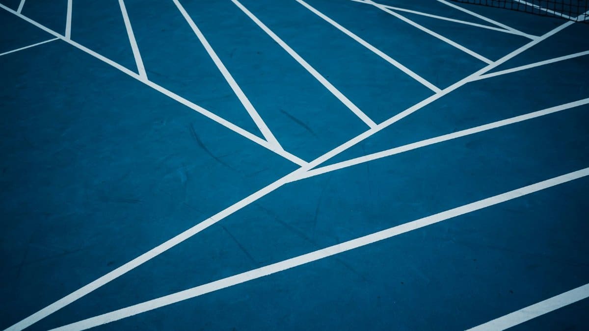 Blue tennis court with abstract white lines creating geometric patterns.